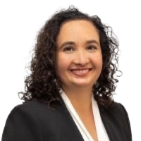 Triada Stampas looks smiling into the camera. She has dark, curly hair and is wearing a suit.
